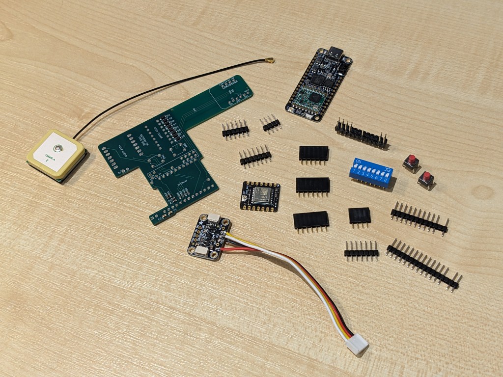 A photo of a collection of electronic components including a printed circuit board, a GPS antenna, some electronic modules, switches, a DIP switch module, and a variety of pin and socket connectors. They are arranged haphazardly.