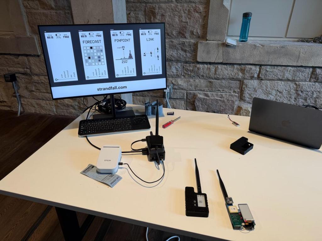 A desk holding a screen, keyboard, receipt printer, a printed receipt, Raspberry Pi, two MFDs, a lithium battery, a screwdriver and a laptop.