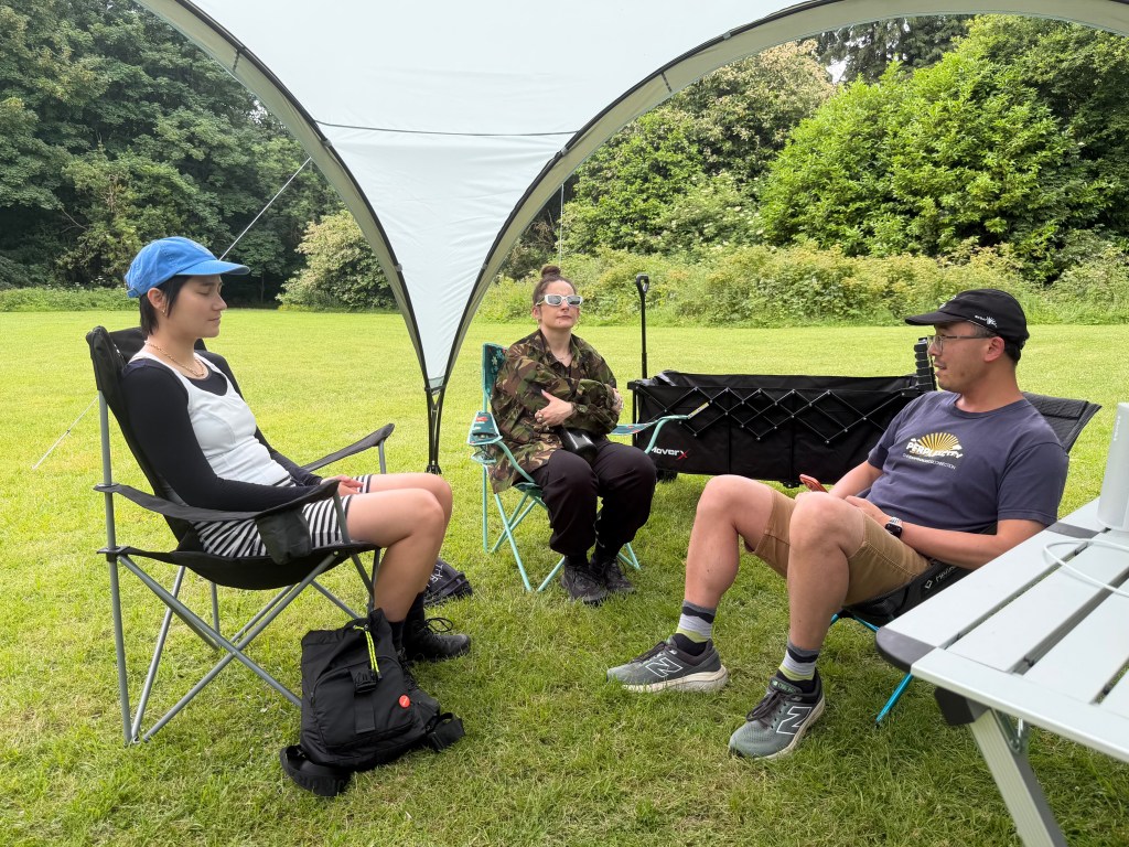 Three people sitting in camping chairs underneath a dome-like gazebo